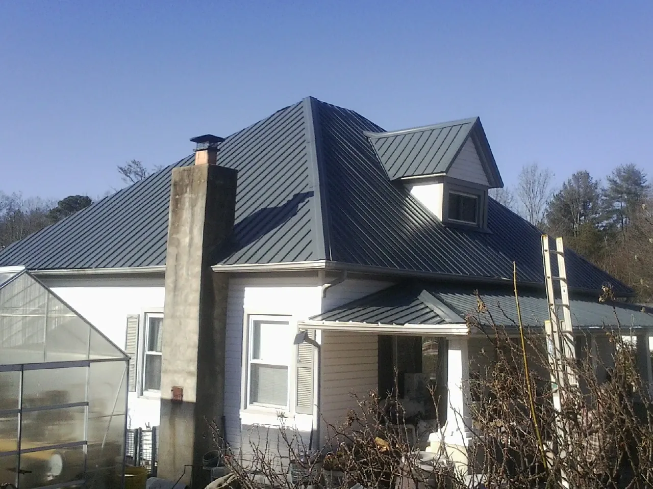 Dark blue standing seam metal roof on a white farmhouse with dormer — Slate & Tile Roof Repair by Roofing Brothers in Cooke City