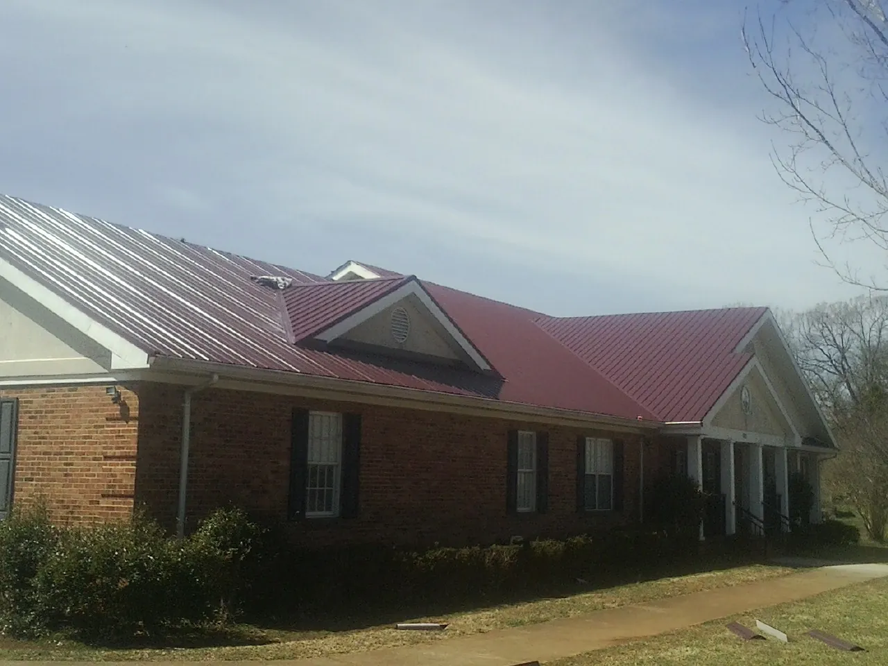 Red metal roof with gabled entries on a long brick building, from a Hail Damage Roof Repair job in Cooke City