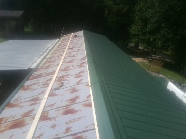 Old rusted panels beside newly installed green metal roofing — Wind Damage Roof Repair by Roofing Brothers in Cooke City