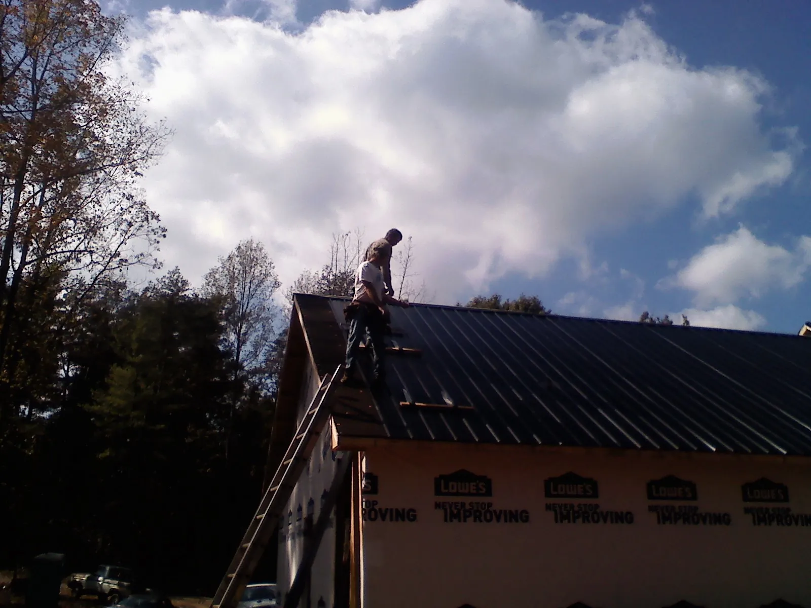 Roofer fastening dark metal panels high against a cloudy sky, from a Roof Inspection job in Cooke City