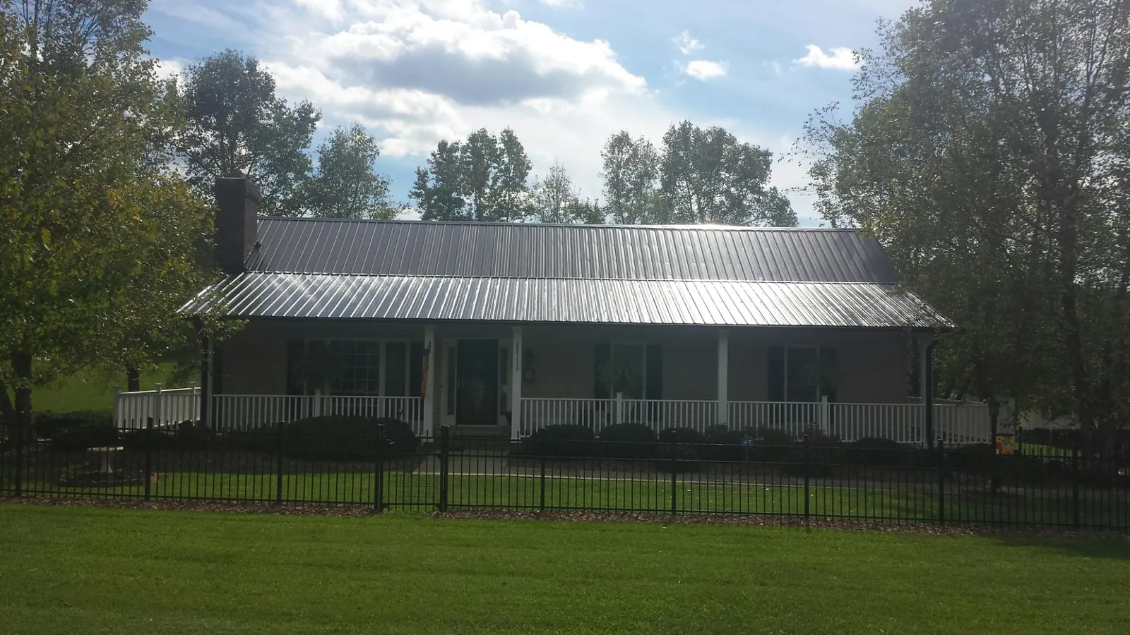 Gray metal roof on a brick ranch with a full width front porch — Gutter Guard Installation work by our crew in Cooke City