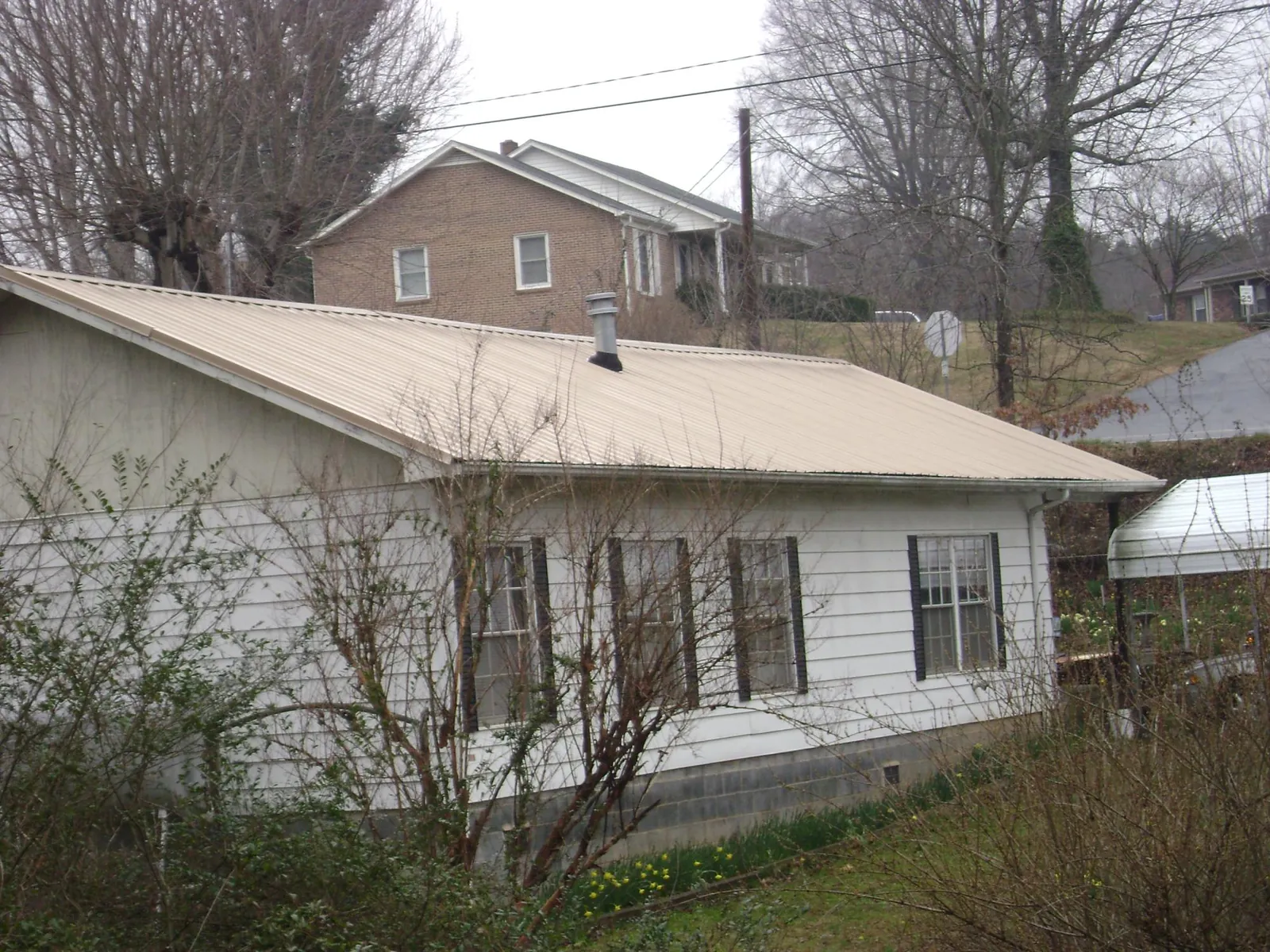 Tan metal roof on a white sided house set into a hillside — Commercial Roofing by Roofing Brothers in Cooke City